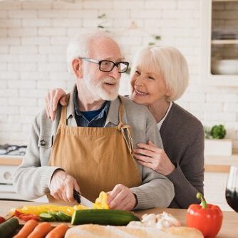 Smiling cheerful happy caucasian senior old elderly couple family grandparents spouses wife and husband cooking together, helping make vegetable